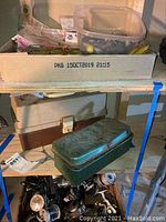 Fishing gear including two tackle boxes stacked plus metal green tackle box and a crate with several fishing reels at bottom shelf.