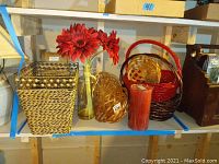 Photo showing six woven baskets, a yellow vase with red faux flowers, and a tall red battery operated candle on a shelf.