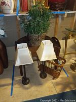 Photo showing drop leaf table with two lamps on floor in front, faux plant on table, and wooden magazine holder on floor
