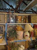 Photo of shelf showing assorted baskets, two glass solar lights, metal lantern, ceramic lamp with shade, and basket with faux plants.