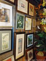 Overview of 7 framed wall art pieces mounted on a wall, featuring floral, botanical, and landscape themes in various frame styles and colors. Shows size variety and frame conditions with scratches.