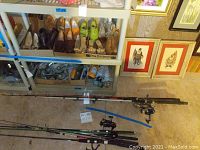 Multiple fishing poles and reels laid on the floor and leaning on shelves. Includes Shakespeare and Lovia reels.