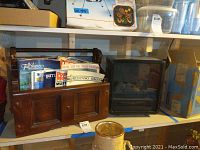 Wooden magazine holder with magazines, black electric fireplace heater, and surrounding shelves with miscellaneous storage items.