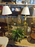 Photo of side table with glass top, two lamps, fireplace tools, faux plant, clock, and vase