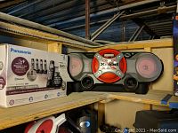 Sony Xplod car stereo radio unit with red and black color scheme and front-facing speakers, placed on a shelf next to the Panasonic phone box.