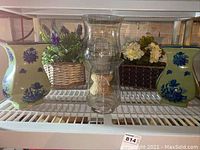 Two matching ceramic vases with blue floral designs, two glass candle holders with woven bases, and two baskets with faux flowers arranged on a metal rack.