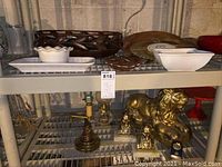 Shelf with various decorative items including carved wood bowl, white ceramic dishes and bowls on top shelf; stone lion figurine, Abraham Lincoln bookends, lamp base, oil lamp on lower shelf