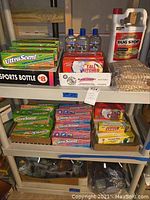 Shelf containing multiple boxes of UltraScent fabric softener sheets, aloe vera gel bottles, trash bags, clothespins, insect killer spray, sports bottle.