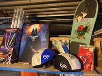 Photo showing boxed LED saber swords, Darth Vader poster behind, skateboard with cartoon character, children's Gijo helmets and helmet covers, and package of tights.