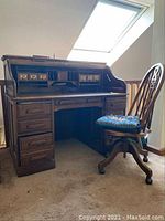 Full view of Oak Crest roll top desk with the wood office chair in front on carpet under skylight.