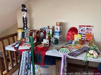 Wide shot showing assortment of holiday decoration items on a table including wooden snowman, wrapping paper rolls, ribbons, and boxes.
