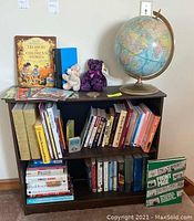Full view of bookshelf containing books, globe on the top right, two teddy bears, and commemorative coin in the center.