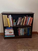 Front view of dark wood laminate bookcase filled with various books on two shelves.