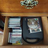 Drawer with a stack of CDs, cassette tapes, and a black plastic Metro cassette holder with handle.