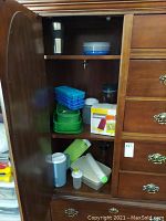 Photo showing inside of wooden cabinet with several plastic food storage containers in blue and green, blue ice cube trays stacked, white popsicle molds, plastic pitcher with green handle and lid, and small plastic containers.