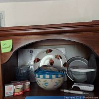 Photo of wooden shelf with clear glass bowls, strawberry design platter, Temptations Old World ceramic mixing bowls stacked inside each other, plastic covered measuring cup, candy thermometer, baking cups and some additional small kitchen items.