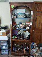 Front view of the tall wooden bookcase showing four shelves filled with miscellaneous kitchenware and other items (not included in the lot)
