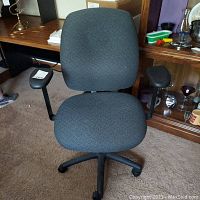 Front view of gray upholstered office desk chair with black plastic armrests and five caster wheels on base. Shows general wear and stains on the fabric upholstery.