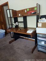 Front angled view of a woodgrain computer desk with adjustable black shelves, showing wear and scratches on the surface.