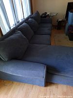 Blue fabric sofa with chaise, shown at a side angle with curtains in the background.