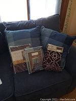 Two blue plaid throw pillows, two packaged curtain panels in front of dark upholstered couch