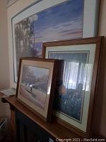 Photo showing three framed country scene prints arranged together on furniture, one very large with white and blue frame, two smaller with wood tones.