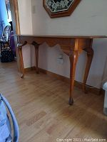 Side angle of wood console table showing cabriole legs and scalloped apron detail.