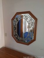 Full view of the octagonal mirror mounted on the wall showing wood frame and floral etched pattern on the glass