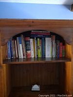 Wooden shelf with assorted cookbooks arranged upright showing bi-fold spine titles and front covers.