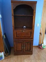 Full view of tall wooden bookcase with an arched open shelf on top, drop front desk in the middle, and two-door cabinet below. Medium brown wood with brass tone hardware.