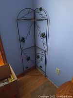 Full view of the green metal wire corner shelf with three tiers and ivy leaf decorations in a room corner.