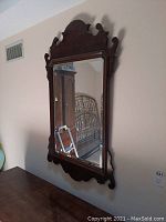 Front view of rectangular wall mirror with decorative dark wood frame and beveled glass mounted on the wall.