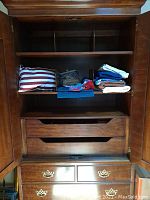 Photo of a wooden cabinet interior containing the striped pillow, folded sheets, and cloth placemats arranged on the shelves.