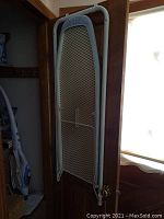 Door hanging ironing board folded up against the door, showing white metal mesh surface and frame.