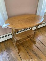 Side angle view showing oval wooden top with scratches, turned legs, drawer with wooden knob, and lower shelf.