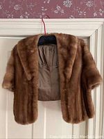 Front view of a brown mink fur stole with short sleeves hanging on a hanger, showing the front and upper part with satin lining visible inside.