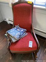 Antique rocker with cranberry upholstery and folded throw blanket placed on the seat