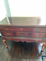 Front view of cedar hope chest showing drawers, brass handles, and queen anne legs on a wooden floor.