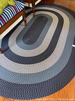 Full view of oval braided rug with concentric color bands on wooden floor