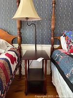 Full view of the brown wooden nightstand with two shelves and attached lamp placed between two beds, showing scratches and general condition.