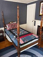 Wide angle of the four-post twin size bed frame with bedding and dark wooden posts visible.