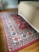 Overview of rug under bed showing red field with central geometric motifs and borders