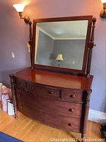 Full frontal view of a dark wooden dresser with an attached large rectangular mirror held by turned posts. Visible wear on wood and mirror reflective surface.