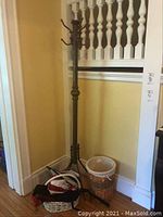Metal coat rack standing upright near wall with wicker basket and umbrella basket on floor