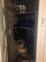 Shelf with Snow Jet spray cans atop, briefcase and basket below with assorted items