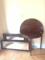 Mirrors and round folding table grouped against a wall on wooden floor, showing their size and shape.