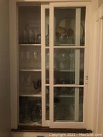 Photo of a cabinet with multiple shelves showing various clear glassware items including wine glasses and water glasses arranged orderly.