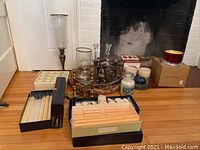 Wide view showing assortment of candles, candle holders, jar candles, boxed tapers, and a round woven tray in front of a fireplace.
