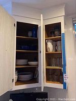 Kitchen cabinet showing shelves with Crate & Barrel white plates, blue and white bowls and glassware mugs on adjacent shelf.