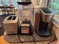 Three small kitchen appliances on granite countertop in kitchen: Breville toaster, Blendtec blender, Keurig coffee maker